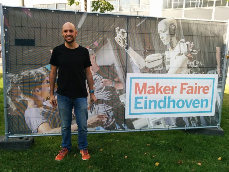 Javier Leiva wearing red running shoes and standing in front of a banner that says Maker Faire Eindhoven