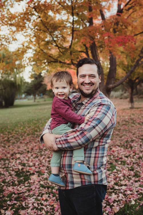 Brett Dery, holding his young son in front of colorful autumn leaves