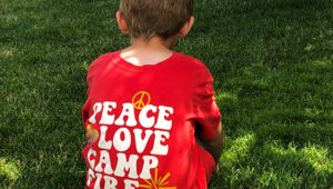A young camper wearing a red Peace, Love, Camp Fire t-shirt.