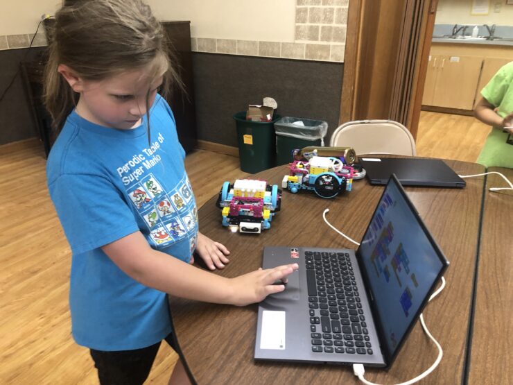 A young programmer stands at a laptop programming actions for her LEGO robot.
