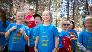 A camper outside at Tumalo Day Camp wearing their bright blue Eat Sleep, Camp Fire, Repeat t-shirts