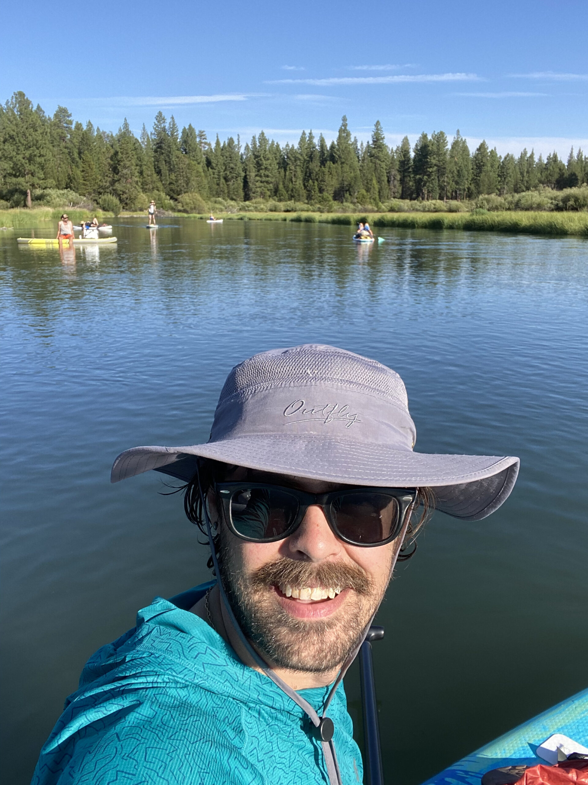 Adam Foster smiles broadly in a an outdoor photo in a kayak on a river