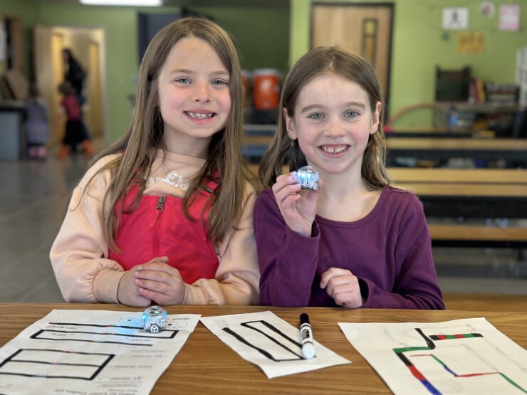 Two afterschool kids pose with their Ozobots and project worksheets