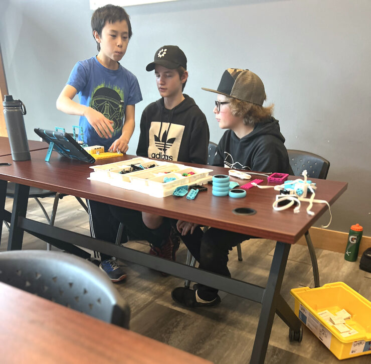 three youth strategizing next steps while working on robotics challenges at Bit(e) of Robotics at Deschutes Public Library.