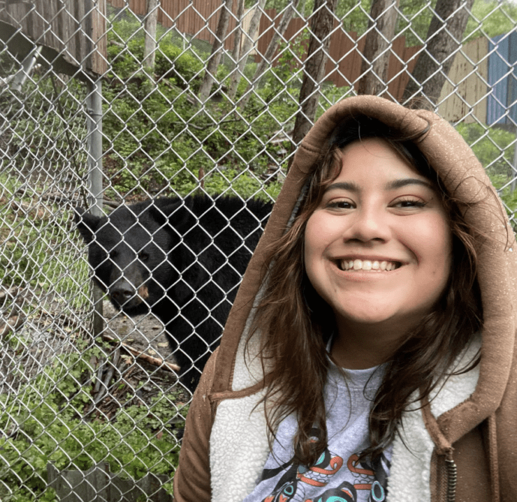 Cyprianna stand in front of a fence behind which is a bear.