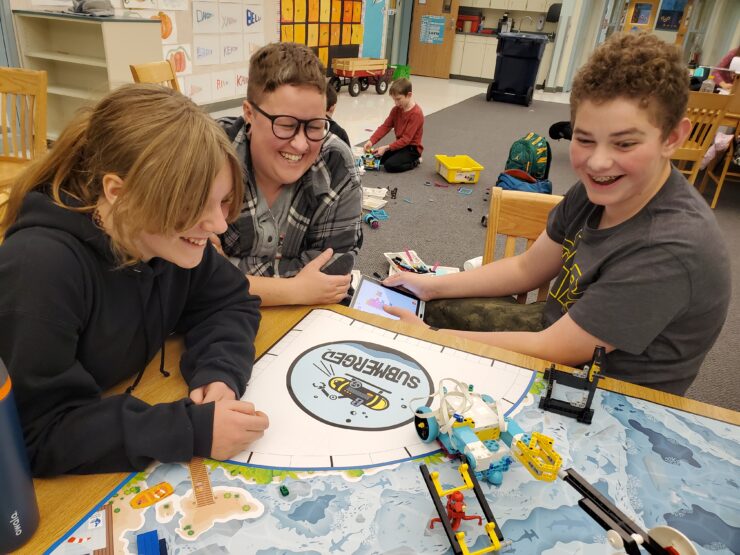 Robotics instructor smiles over kids looking at robot on a course.