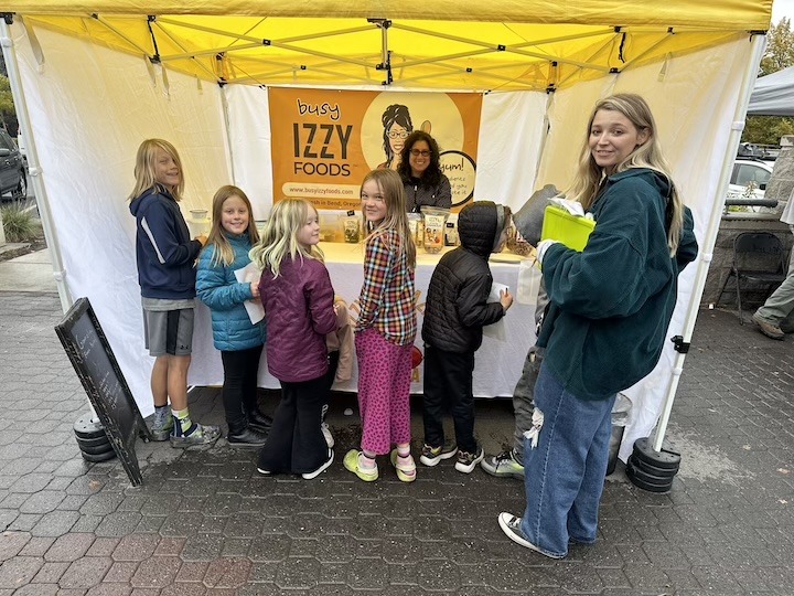 Camp counselor stands with youth in front of a farmer's market booth.