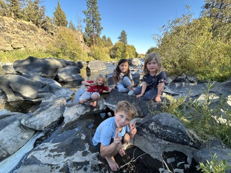 Four kids playing on rocks in a stream.