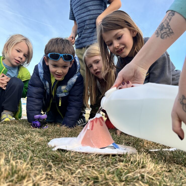 Youth surround a volcano experiment on the playground.