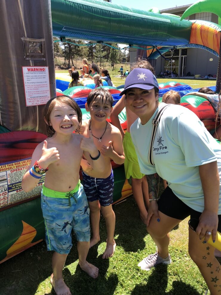 Summer camp counselor poses with youth by waterslide.