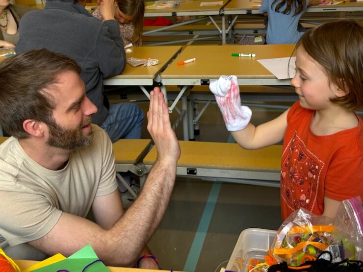 Andrew Blaylock high-fiving a youth and her sock puppet.