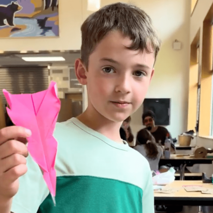 Boy holding two paper airplanes taped together.