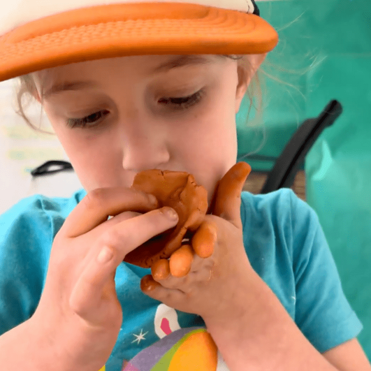 Girl smelling orange clay pinch pot.