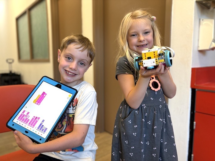 Two youth smile as they hold a robot and the ipad for coding.