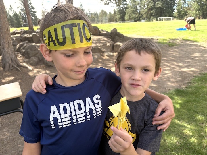 Two SummerKids male youth hugging and holding an Origami parrot.