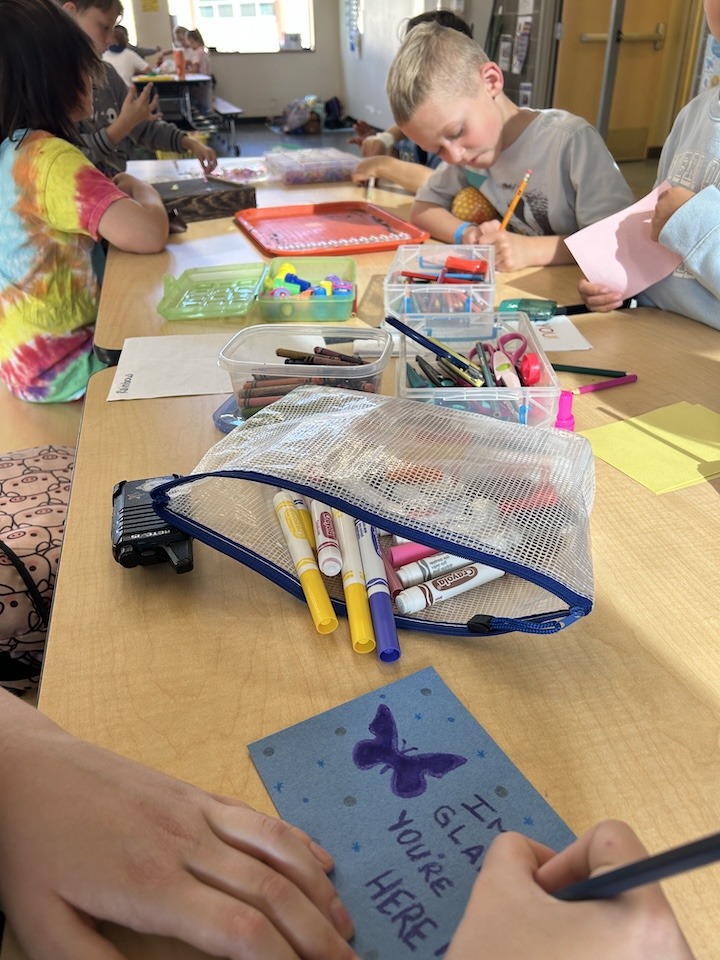 A table with lots of art supplies and kids making cards.