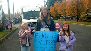 Teen holding Veterans Day sign with two youth alongside her.