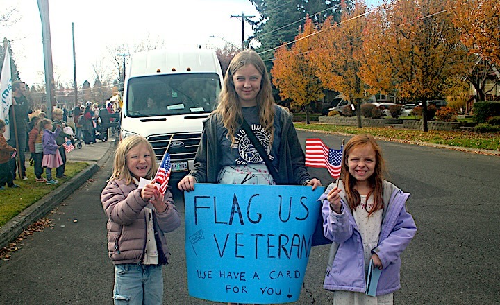 Teen holding Veterans Day sign with two youth alongside her.