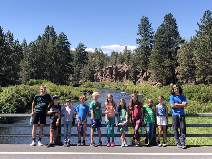 Campers and teen counselors standing on bridge with mountains in background